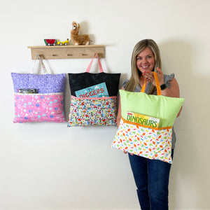 Amanda holding a green dinosaur reading pillow cover with two more pillow covers hanging on a wall shelf