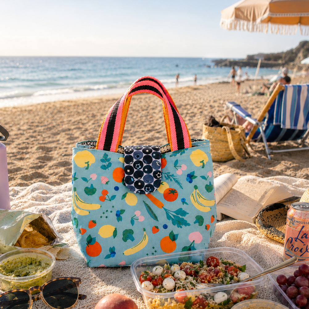 Colorful lunch bag with food and drinks on a sandy beach