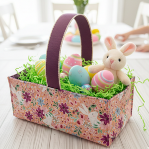 Easter basket with colorful eggs and a plush bunny on a light wooden table.