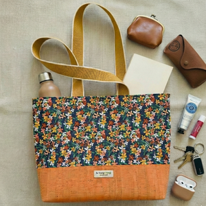 Floral-patterned tote bag with brown accents on a beige surface, surrounded by accessories.
