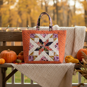 Quilted bag with floral pattern on a wooden bench with pumpkins and autumn leaves.
