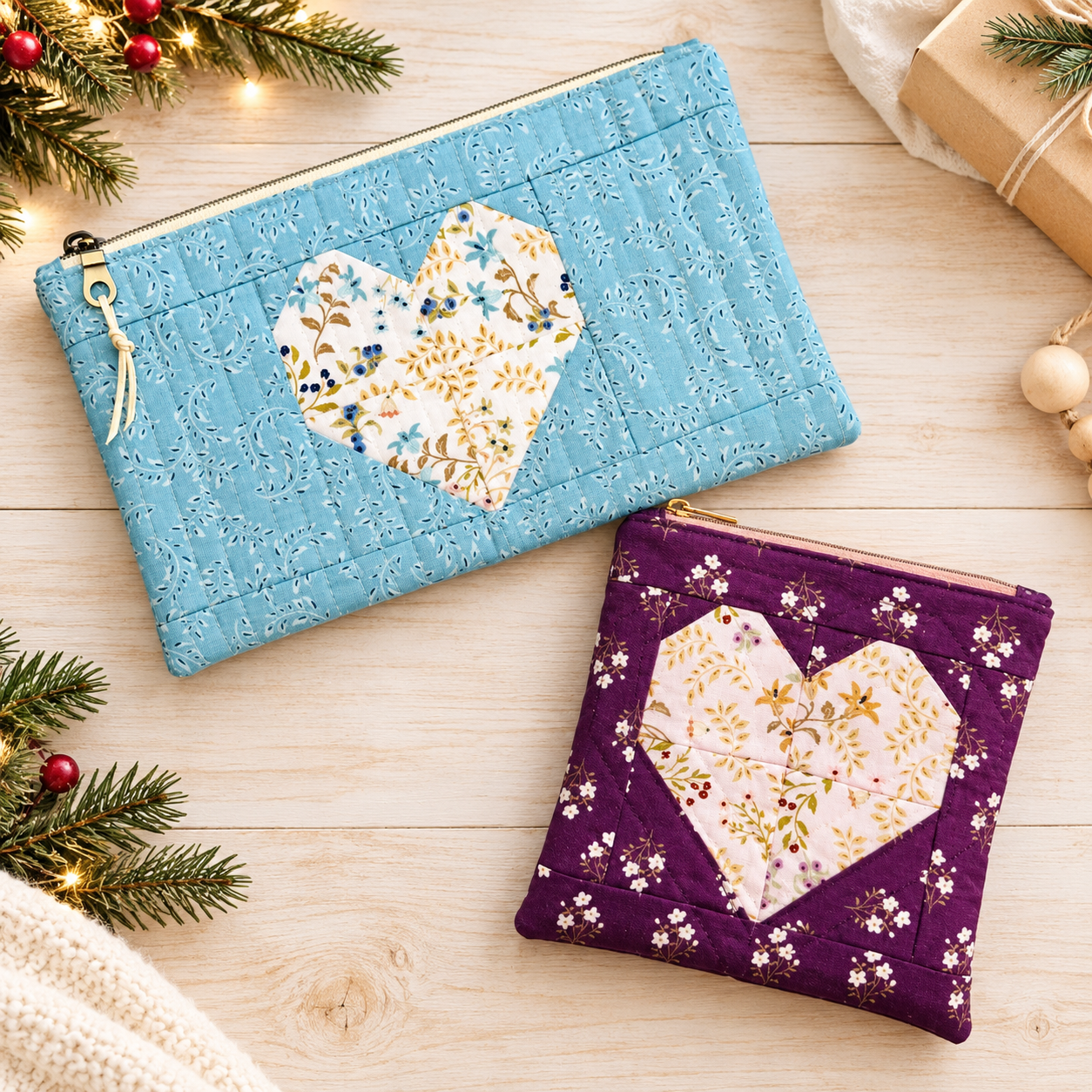 Two Heartfelt pouches, a large blue and a small purple, each with a patchwork heart, among holiday greenery