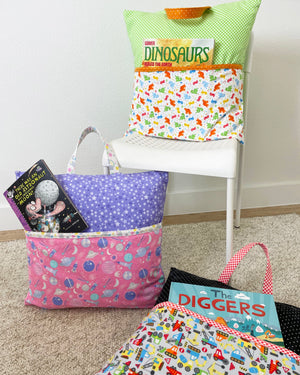 Three handmade reading pillow covers in dinosaur, space, and transportation prints styled with books and toys