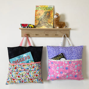 Three handmade reading pillow covers in transportation, dinosaur, and space prints hanging on a wall rack