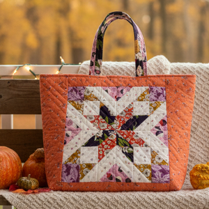 Quilted tote bag with floral pattern on a wooden bench with pumpkins and autumn leaves.