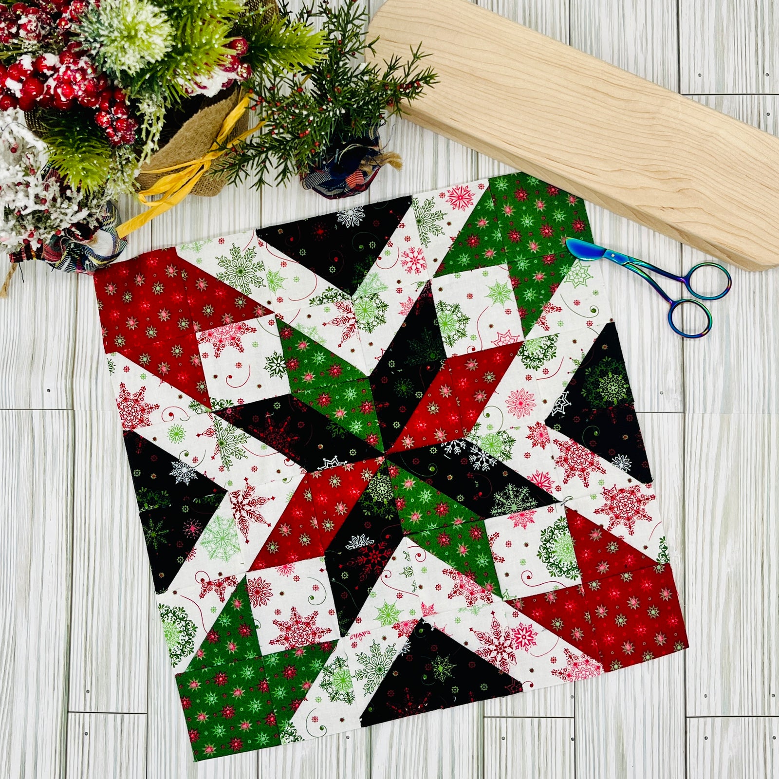 Star quilt block pattern in red green black and white holiday prints with fabric scissors and wooden board