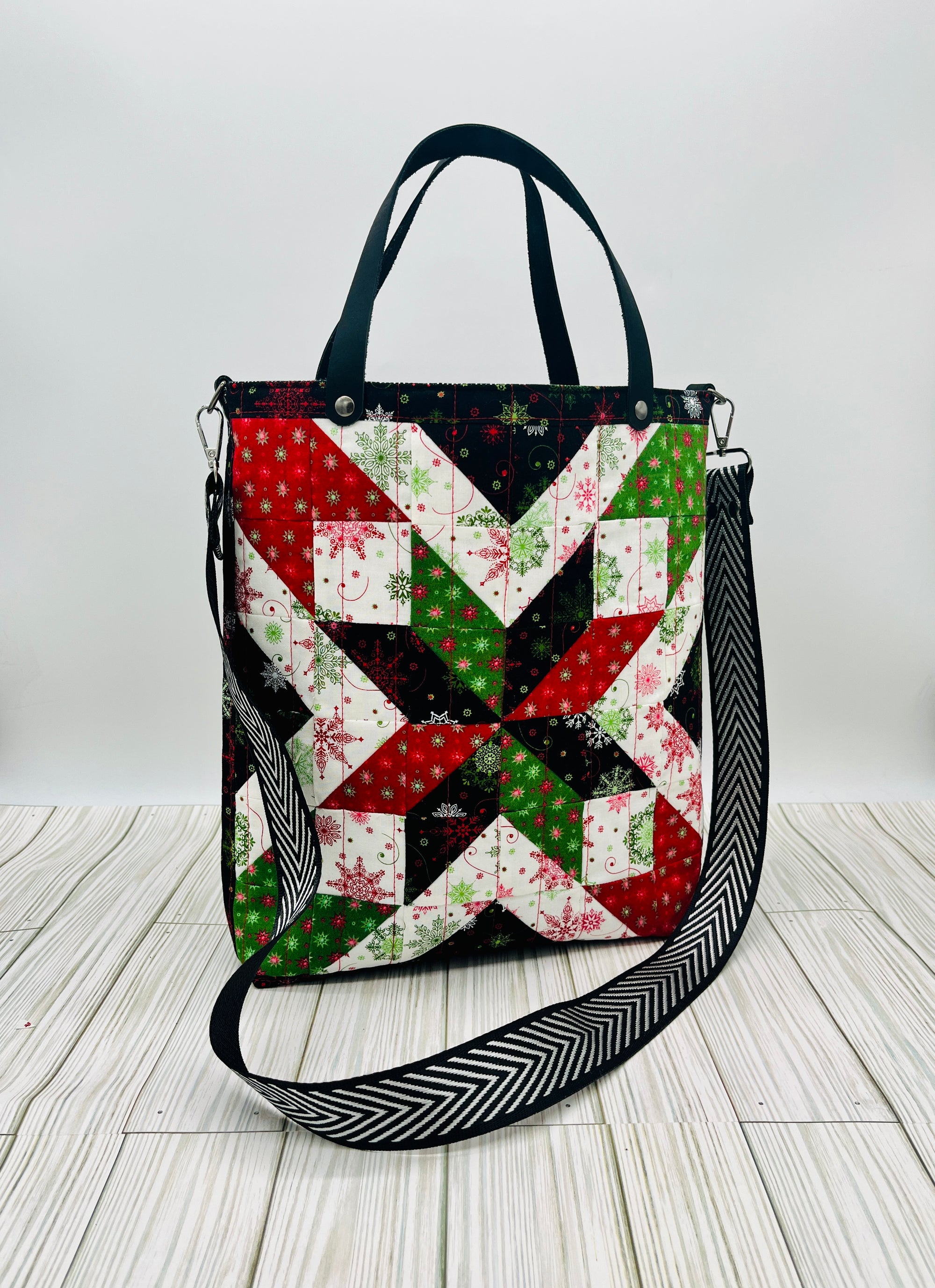 Holiday-themed tote bag featuring a red green and white star quilt block pattern with black straps