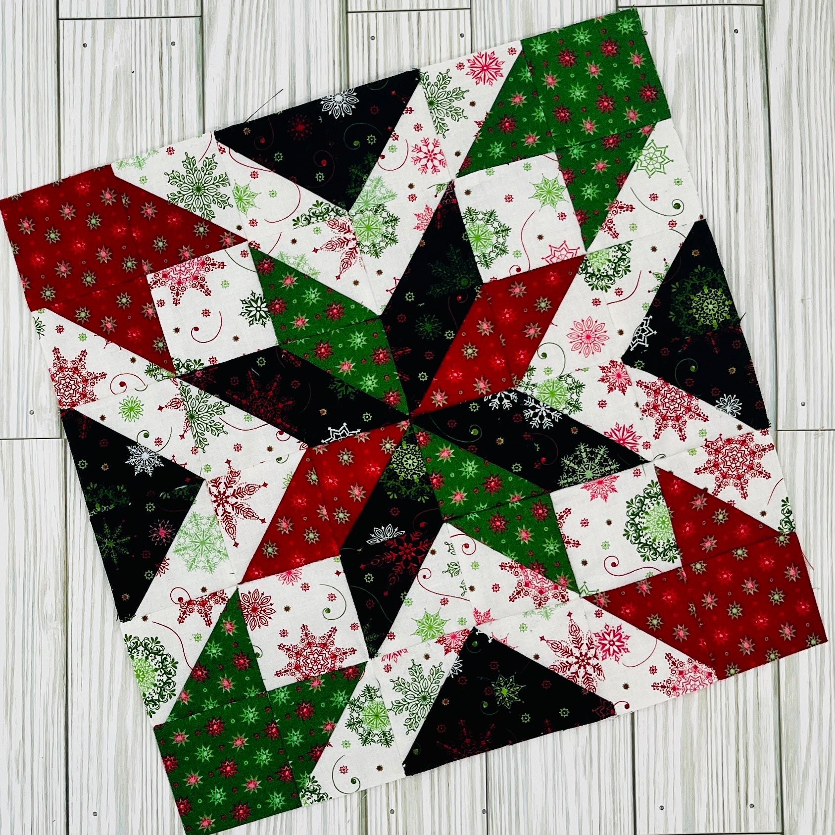 Colorful star quilt block pattern in red green black and white holiday fabrics on wood background