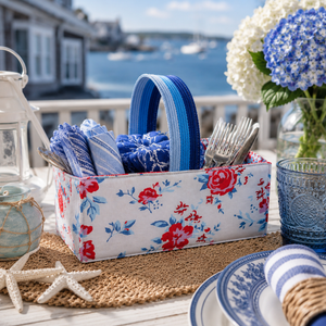 Floral-patterned gifted stitches basket with blue and white items on a table by a waterfront.