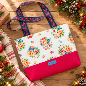 Joanna tote in a white floral print with a pink base and blue embroidered ribbon handles, styled with pine, pinecones and a red-striped holiday towel