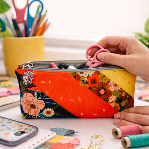 Colorful patchwork pencil case with floral patterns held by a hand on a desk with stationery items.