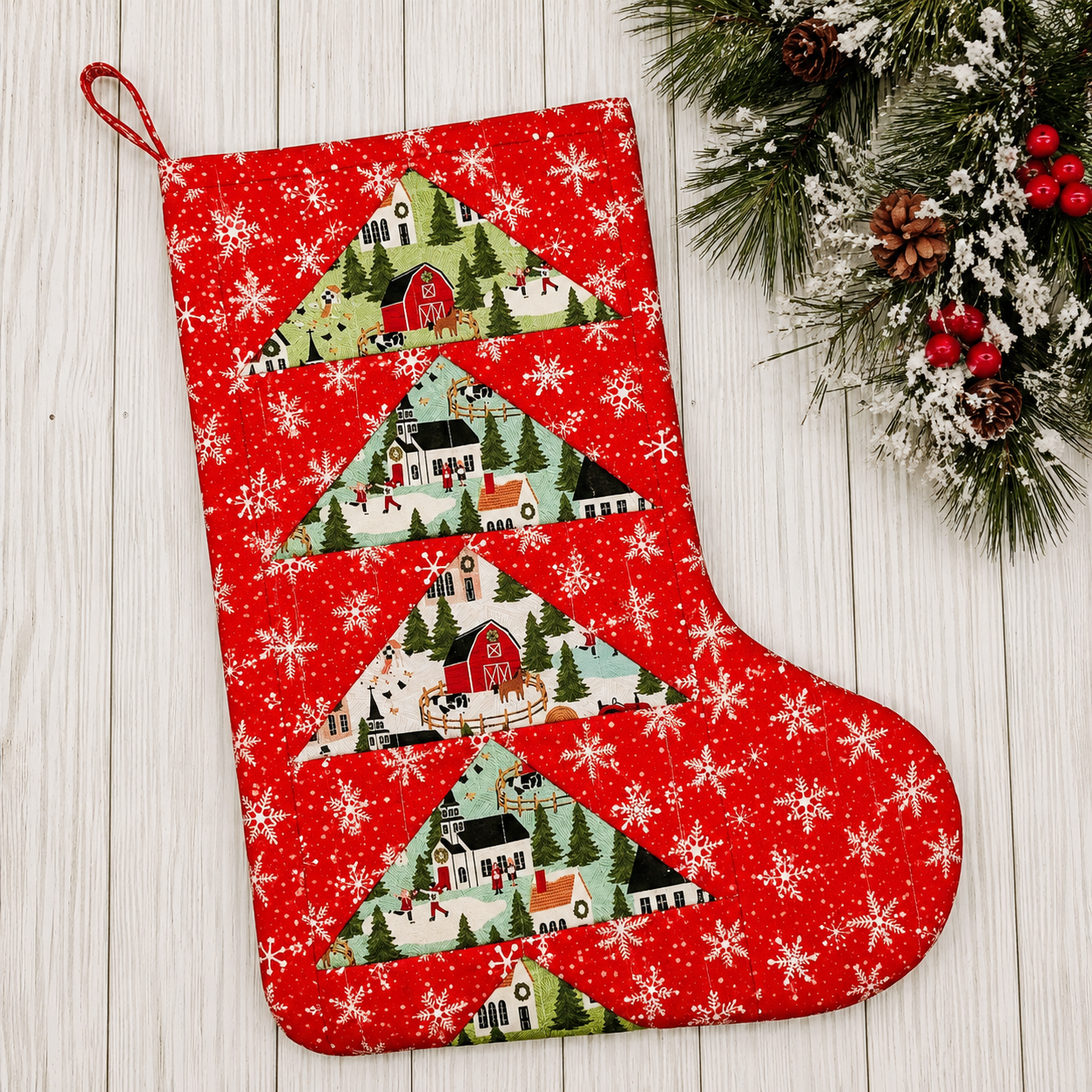 Red Christmas stocking with festive village design on a wooden surface with greenery.