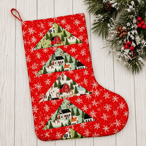 Red Christmas stocking with festive village design on a wooden surface with greenery.
