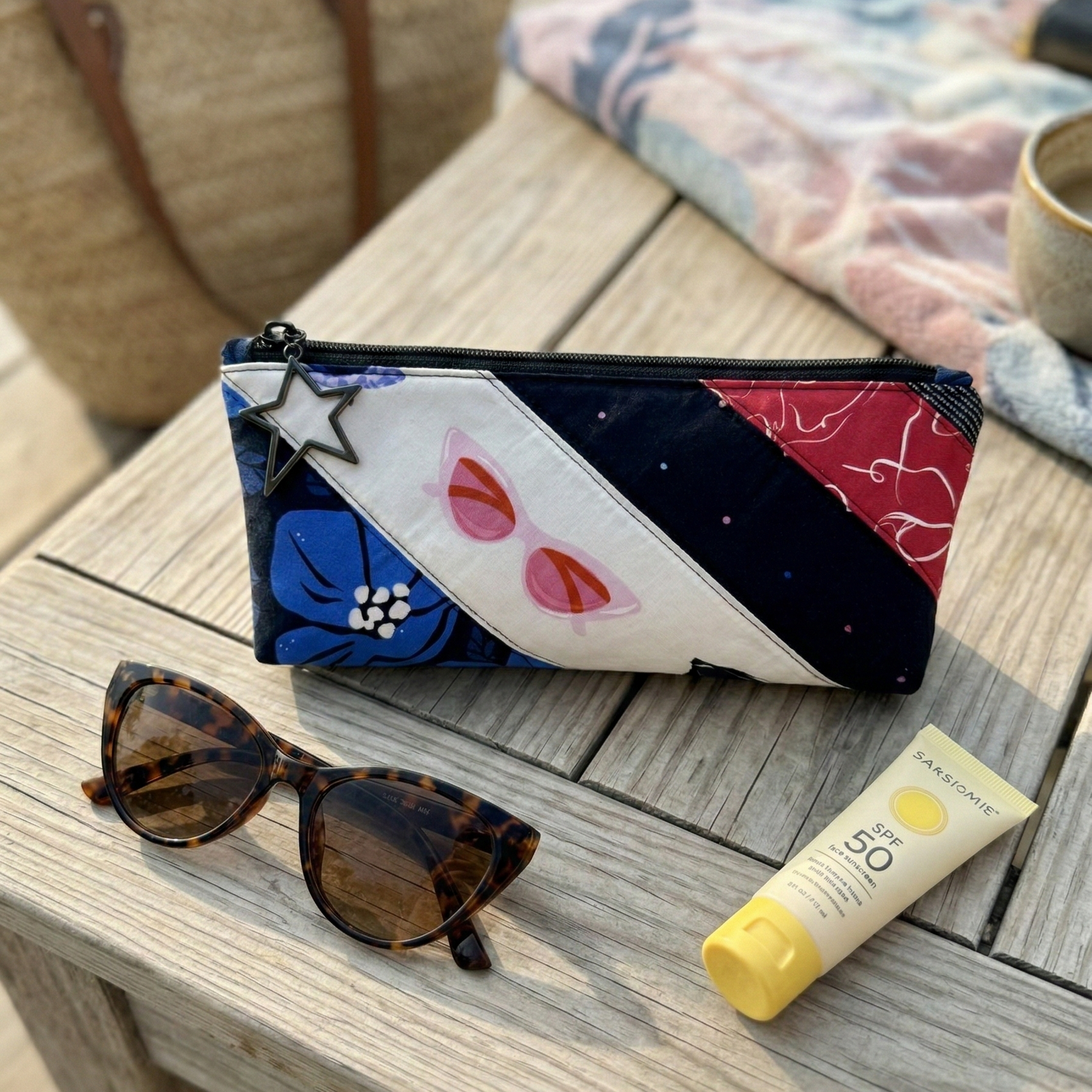 Colorful pouch with floral and abstract designs on a wooden surface with sunglasses and sunscreen.