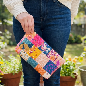 Person holding a colorful patchwork clutch outdoors with plants in the background